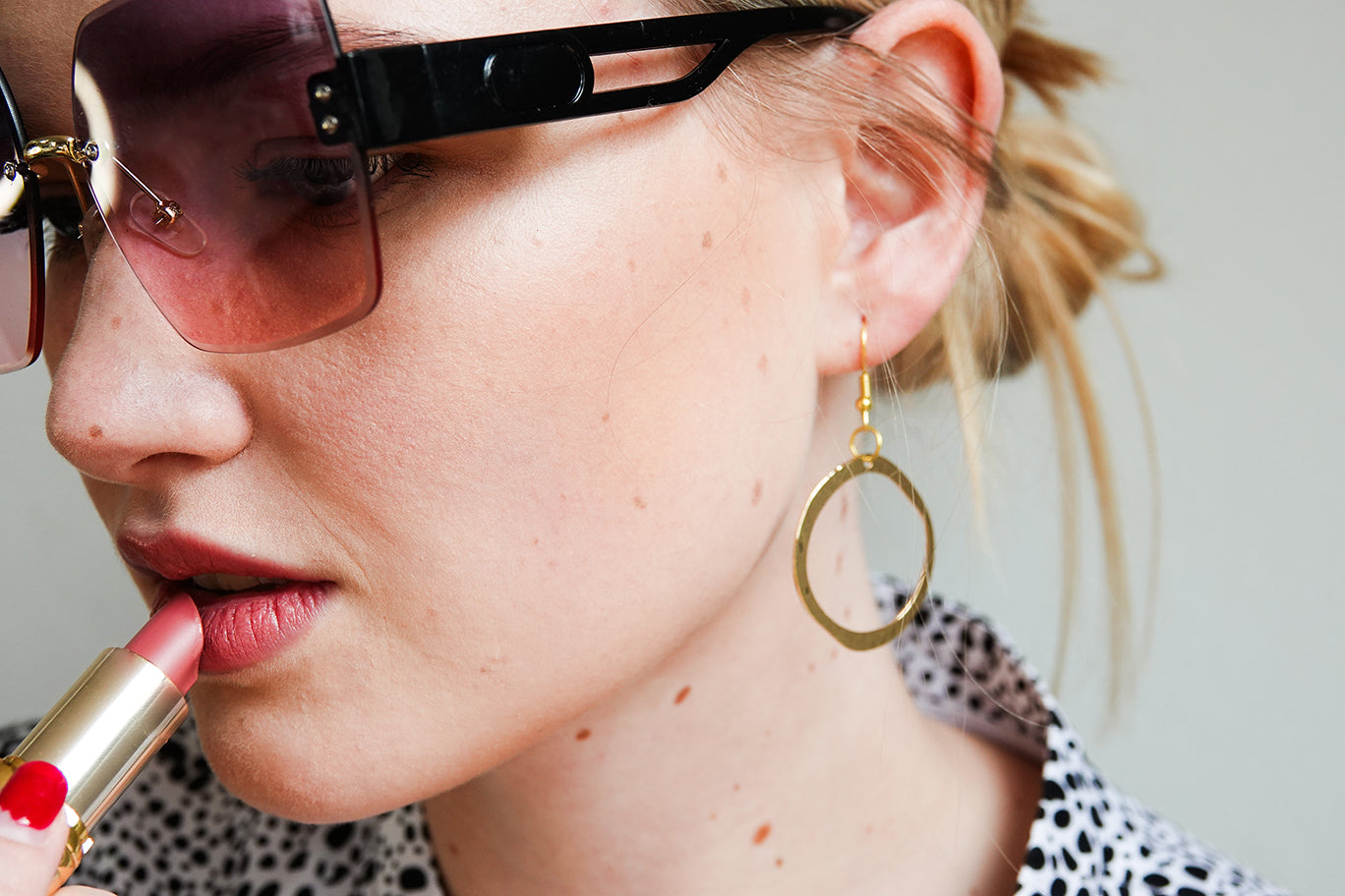 Woman applying lipstick with sunglasses and hoop earrings